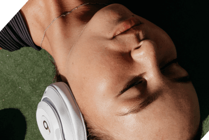 Close-up of a young woman resting her head, eyes closed and expression relaxed, wearing white headphones.