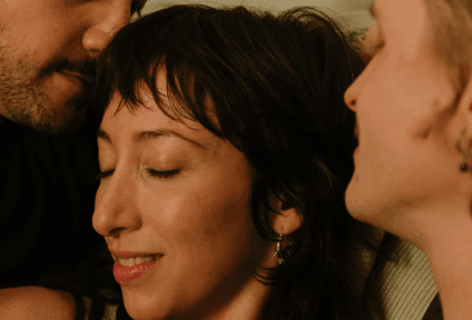 Woman with tan skin and dark hair, eyes closed, enjoying a moment between two partially visible people.